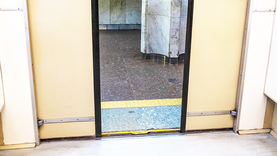 A narrow strip of offset grid DWPs are embedded in a marble floor outside the open doors of an older subway.