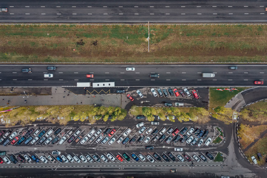 A long thin parking lot abuts a very large road.