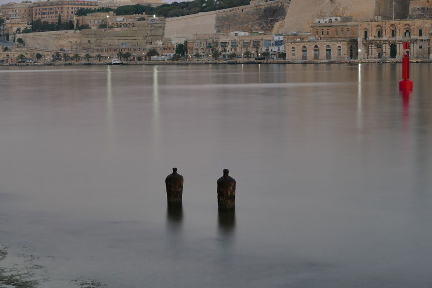 Two rusty cannon bollards stick out of the calm surface of a river