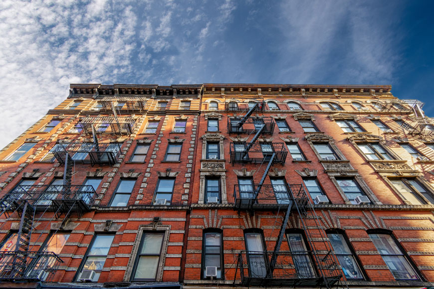 A colorful brick tenement façade is ornamented by wrought iron fire escapes