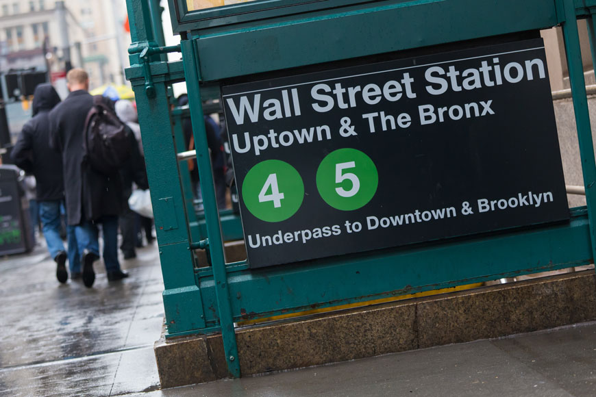 A green enclosure around stairs descending to the subway announce Wall Street Station