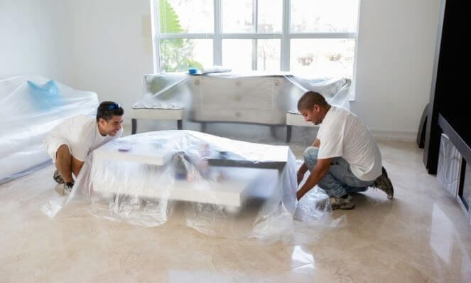 A team applying plastic cloths to furniture to protect it from dust and debris when prepping to remove popcorn ceiling texture.