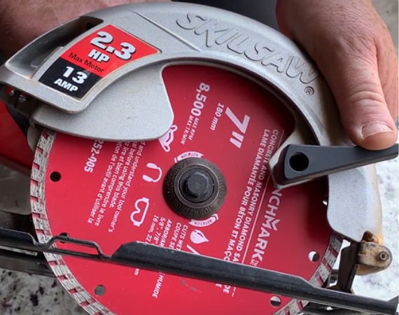 Repair technician supporting the body, upper housing, and lever of a circular saw that has a red-colored diamond-tipped blade