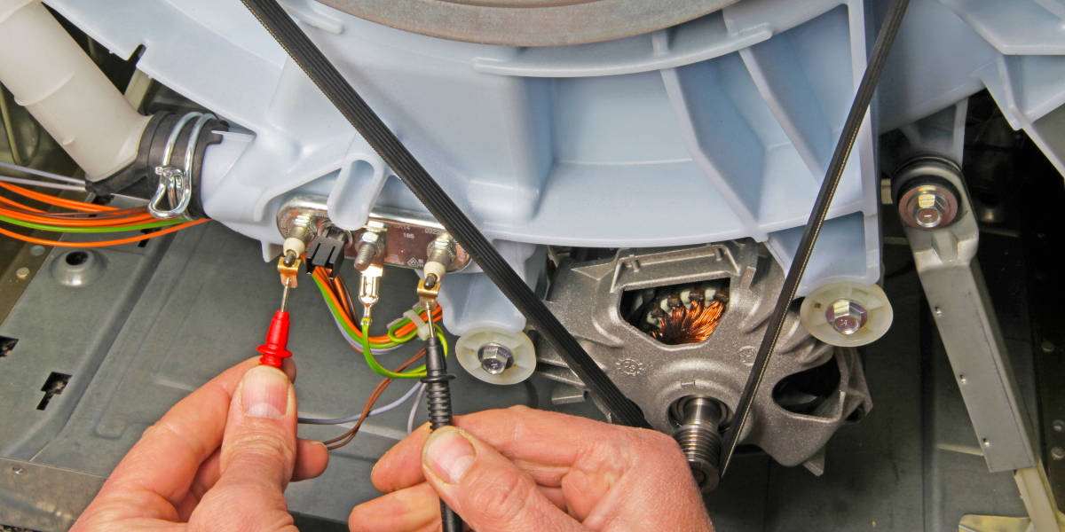 A person uses a multimeter to test electronics in a dryer.