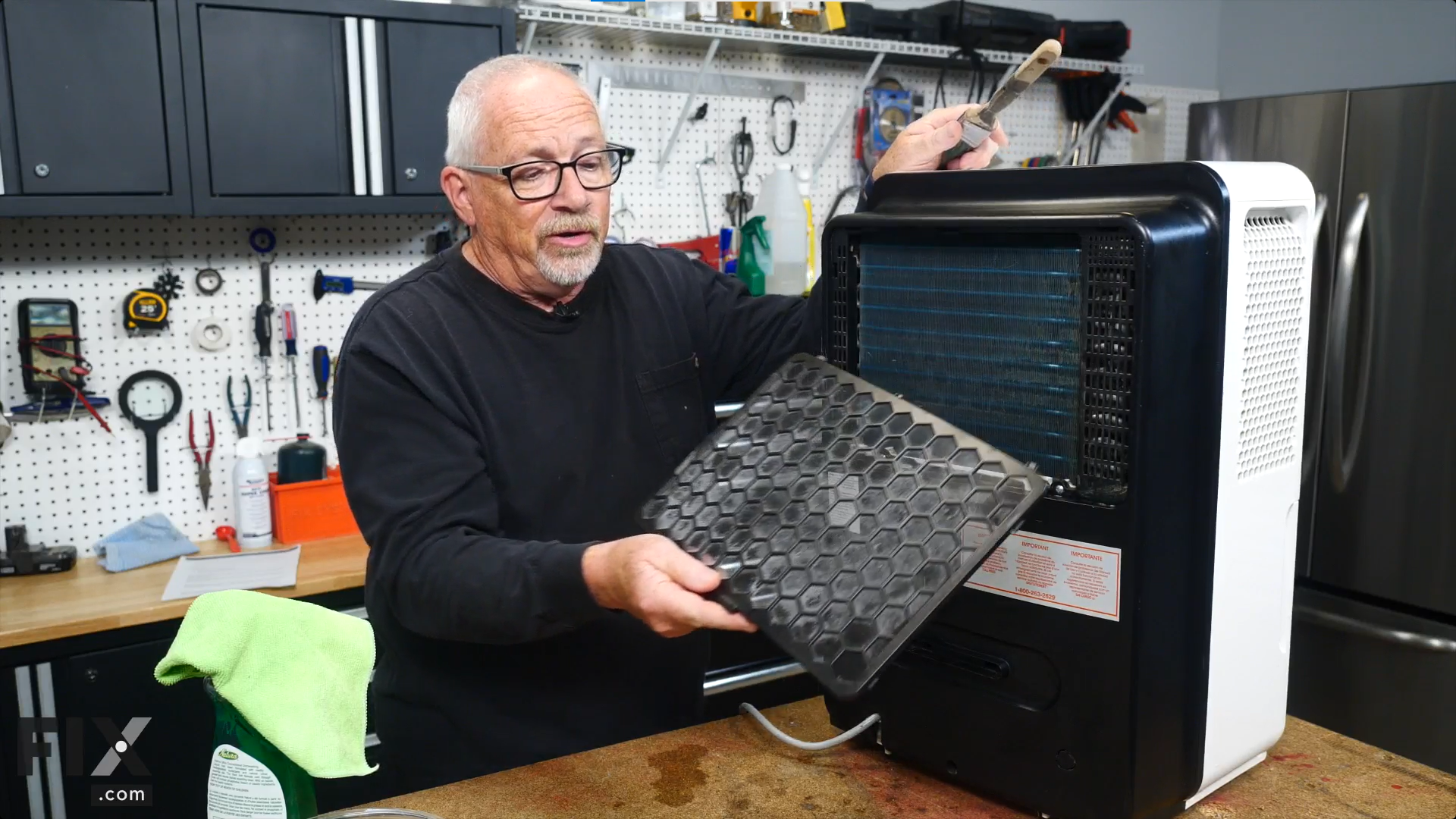 A repair technician removing a dusty black filter from the back of a dehumidifier to clean it with a soft-bristle brush.